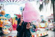 Beautiful model or cute and pretty student woman holds out guilty pleasure, huge pink cotton candy, eats with appetite with fingers, at festival or carnival during summer vacation trip