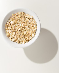 Oat cereal grain. Grains in a bowl. Shadow over white table.