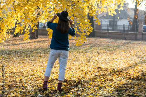 Fotografie, Obraz Woman with a hat leaning back under a tree with a yellow leaves