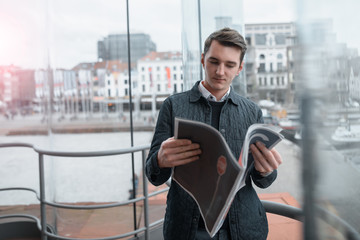 A young guy reads a newspaper inside.