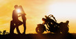 Couple silhouette kissing at sunset and have a big bike parked on the street.