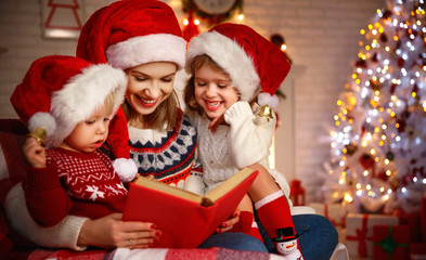 Wall Mural - family mother and children read a book at christmas near fireplace at home
