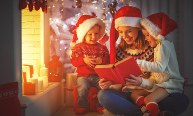 Wall Mural - family mother and children read a book at christmas near fireplace at home