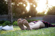 Hipster Asian woman bare foot relaxing to lying on the green grass and putting the white shoes on the ground at the park