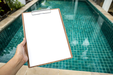 Wall Mural - Girl hand holding blank paper clipboard over clear swimming pool water background