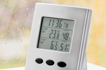 Wall Mural - Weather station device with weather conditions inside and outside. Background of a window with raindrops. Yellow background, golden autumn. Selective focus