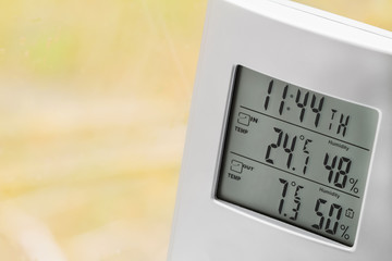 Wall Mural - Weather station device with weather conditions inside and outside. Background of a window with raindrops. Yellow background, golden autumn. Selective focus