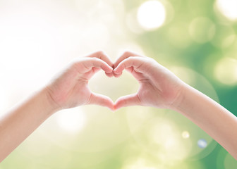 Heart-shape hand gesture of kid's body language for children's love, peace, kindness and world humanitarian aid concept. Hand isolated on sky with green bokeh and sun flare