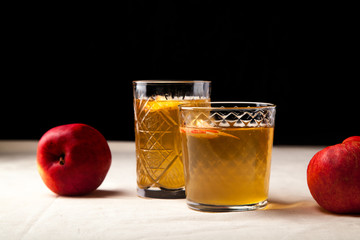 Two vintage glasses with apple cider on black background. Christmas beverages concept. Two red apples and rosemary sprig aside.  Warm backlight. Horizontal composition. Side view.