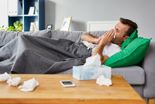 Sick Man Lying On Sofa At Home And Blowing Nose