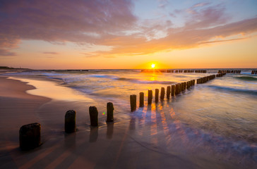 Wall Mural - sunset over the sea beach, waves crashing on the stakes
