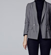 Woman wearing stylish outfit with black turtleneck, gray elegant double-breasted blazer and black skinny jeans. Closeup on fashion details isolated on gray background. Copy space. Negative space.