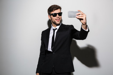 Sticker - Cool bearded guy in black suit and suglasses taking selfie on mobile phone