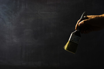 Aufkleber - Hand holding old brush for paints  in fingers with blackboard behind.