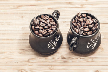 two toned cups with coffee grains on wooden plank background for two