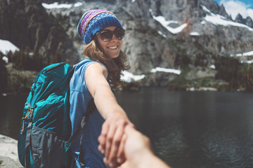 Wall Mural - Young hiking couple with backpacks traveling, woman guiding by the hand into mountain wilderness