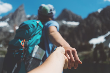 Wall Mural - Young active hiking couple with backpacks traveling, woman guiding by the hand into mountain wilderness