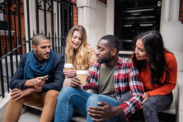 Multiracial group of friends having fun together in London. Two girls and two boys, talking and laughing. Residential district with houses and cars on background. Lifestyle and friendship concepts.