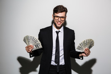 Sticker - Close-up portrait of handsome smiling man in glasses holding bunches of money in two hands, looking at camera