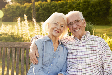 Senior Couple Sitting On Garden Bench In Evening Sunlight