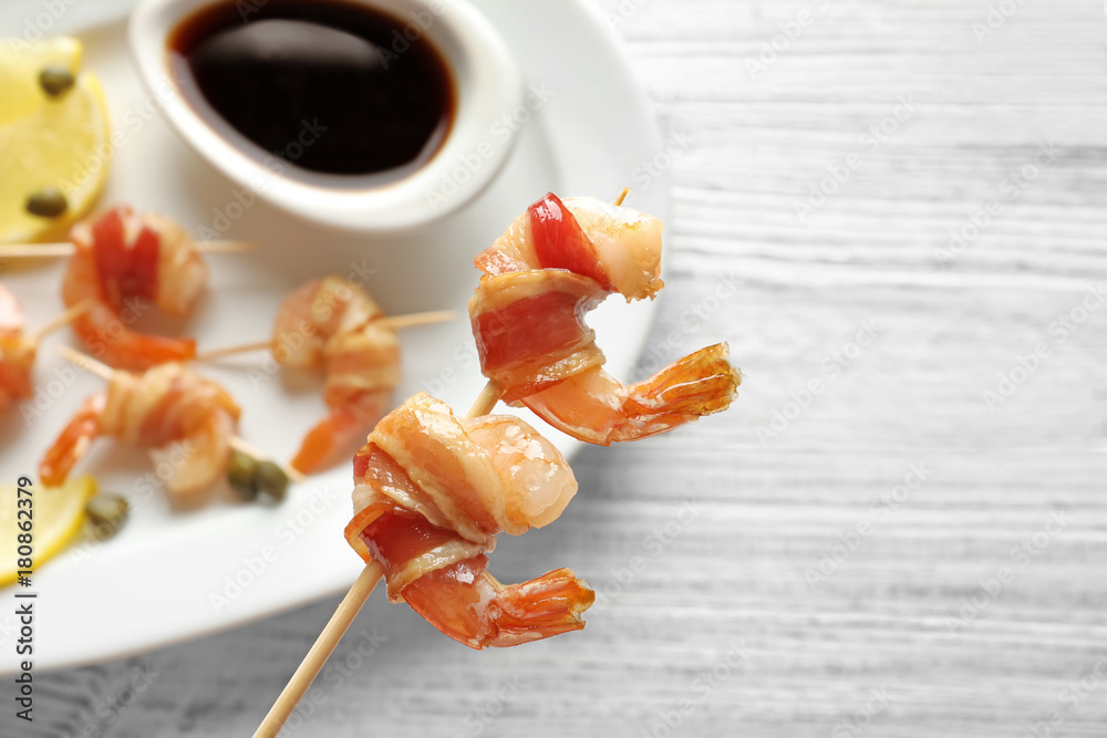 Bacon-wrapped shrimps on skewer over plate, closeup