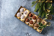 Variety of homemade dark chocolate truffles with cocoa powder, coconut, walnuts as Christmas gift in golden box with fir tree, Christmas decorations above over blue background. Top view, copy space.