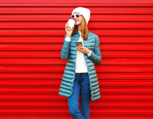 Wall Mural - Fashion young woman drinks coffee using smartphone on a red background in the city