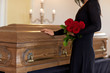 sad woman with red roses and coffin at funeral