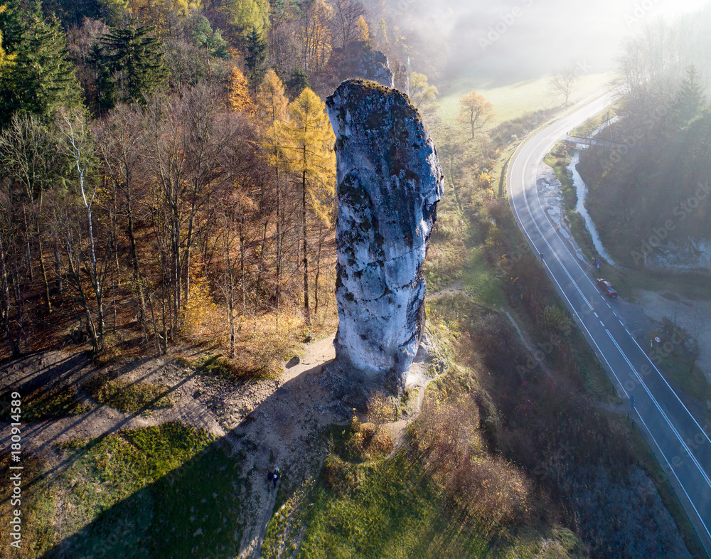 Limestone monadnock, rock called “Maczuga Herkuklesa” (Hercules cudgel or bludgeon) in Pieskowa Skala near Krakow in Poland. Aerial view in fall, in sunrise light through the morning fog - obrazy, fototapety, plakaty 