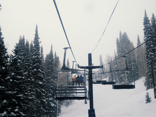 Winter snow on ski resort mountain while riding on a chairlift in the sky.  Cold blue day with white landscape on winter vacation.