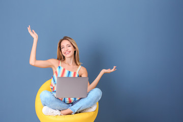 Wall Mural - Young woman with laptop in armchair against blue background