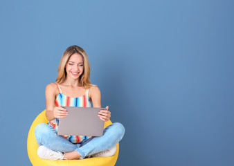 Wall Mural - Young woman with laptop in armchair against blue background