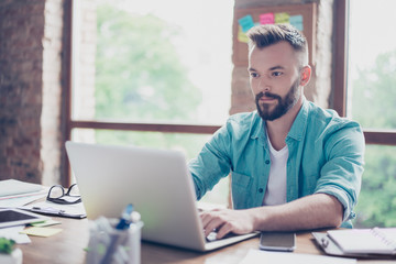 Close up of ponder freelance worker, wearing casual smart, concentrated, focused, serious, sitting at the work place, looking in the laptop screen, typing data