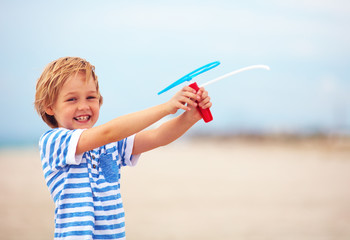 Wall Mural - delighted cute young boy, kid having fun on sandy beach, playing leisure activity games with propeller toy