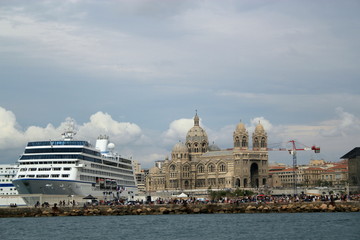 view of a cruise ship set against the cathedral in marseille, with cranes and other boats