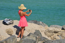 A Woman Wearing A Pink Sundress And A Straw At Taking An IPhone Photograph Of The Beach At South Pointe Park In Miami Beach,Florida