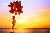 Fototapeta  - happiness or dream concept, silhouette of happy woman jumping with multicolored balloons at sunset on the beach