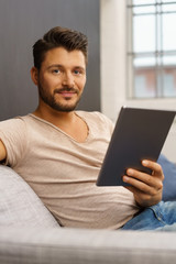 Wall Mural - mann sitzt auf dem sofa und hält sein tablet in der hand