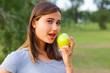 © Alexander - Beautiful teenage girl biting an apple, against green of summer park.