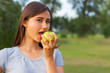 © Alexander - Beautiful teenage girl biting an apple, against green of summer park.