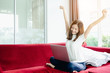 © jumlongch - Asian teenage girl using a laptop computer to check her orders online, and relax on a red sofa in her home.