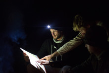 Three Men Looking At Map, At Night, Using Headlamp For Light
