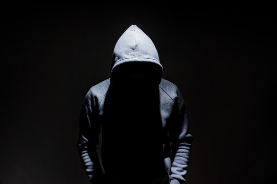 Fototapete - Silhouette of man in the hood, dark mysterious man hoodie, murderer, hacker, anonymus on the black background with free space