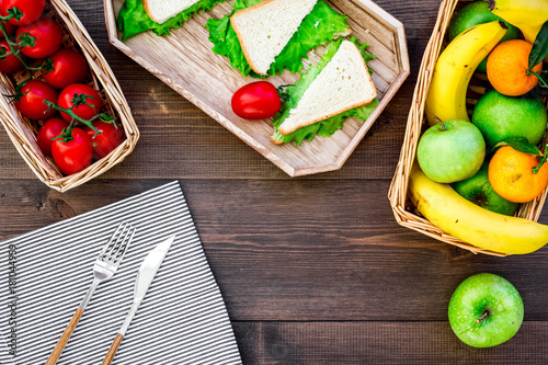 Zdjęcie XXL Co przynieść na piknik. Sanwiches, owoc, warzywa na tablecloth na ciemnym drewnianym tło odgórnego widoku copyspace