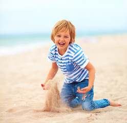 Wall Mural - happy, delighted kid, boy having fun , playing in sand on the beach