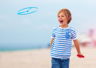 Wall Mural - delighted cute young boy, kid having fun on sandy beach, playing leisure activity games with propeller toy