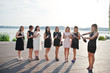 © AS Photo Family - Group of 8 girls wear on black and 2 brides at hen party against sunny beach drinking champagne.