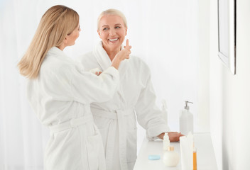 Wall Mural - Mature woman with daughter using cosmetic products in bathroom