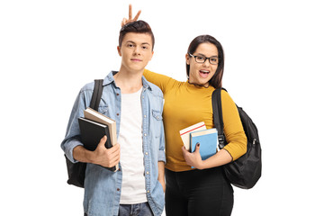 Wall Mural - Female teen student pranking a male teen student with bunny ears