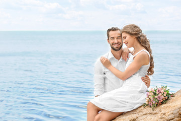 Wall Mural - Happy newlywed couple sitting on rocky beach